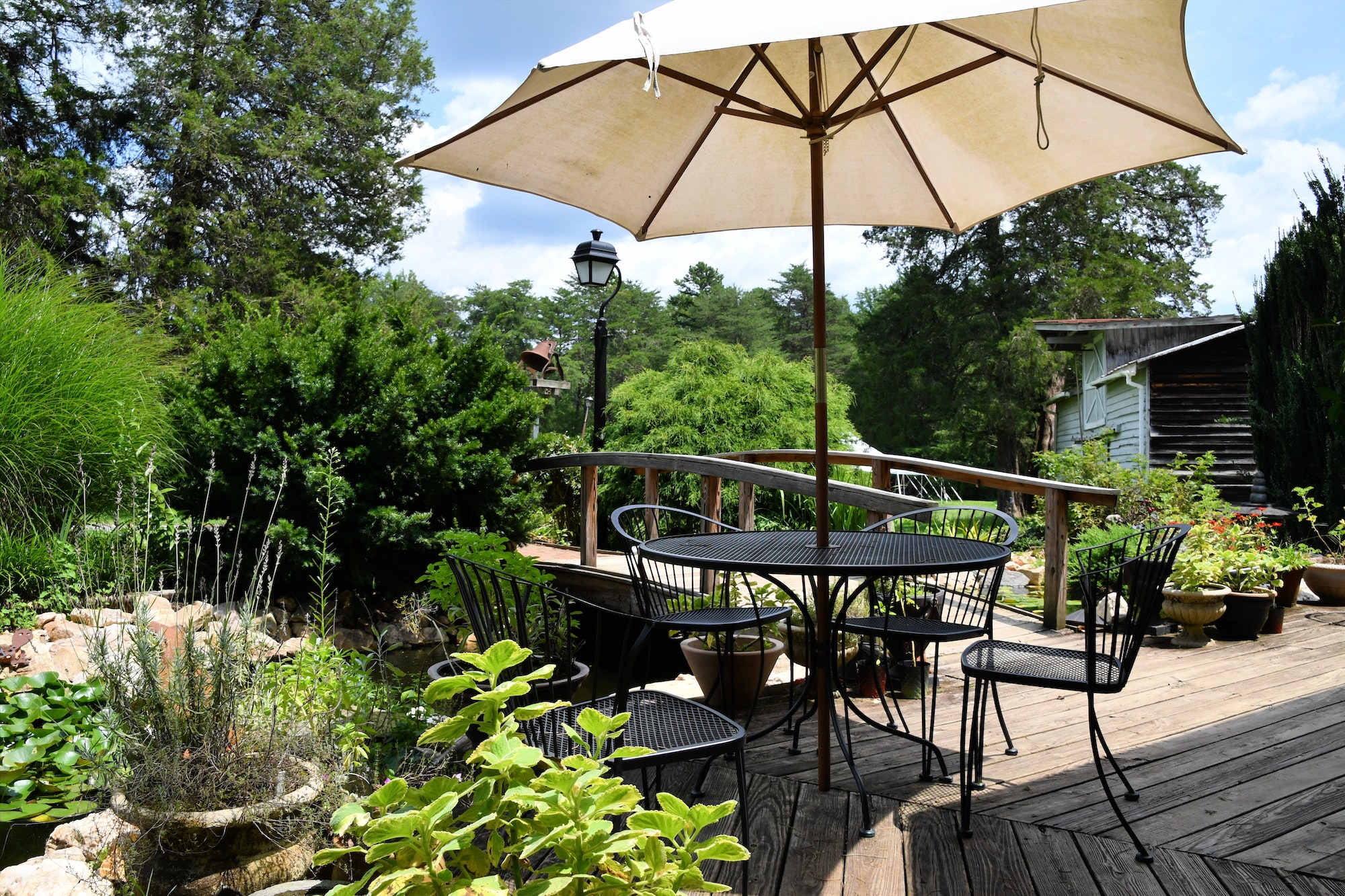 A cozy backyard outdoor living space with a table and umbrella on a deck next to a pond landscaping